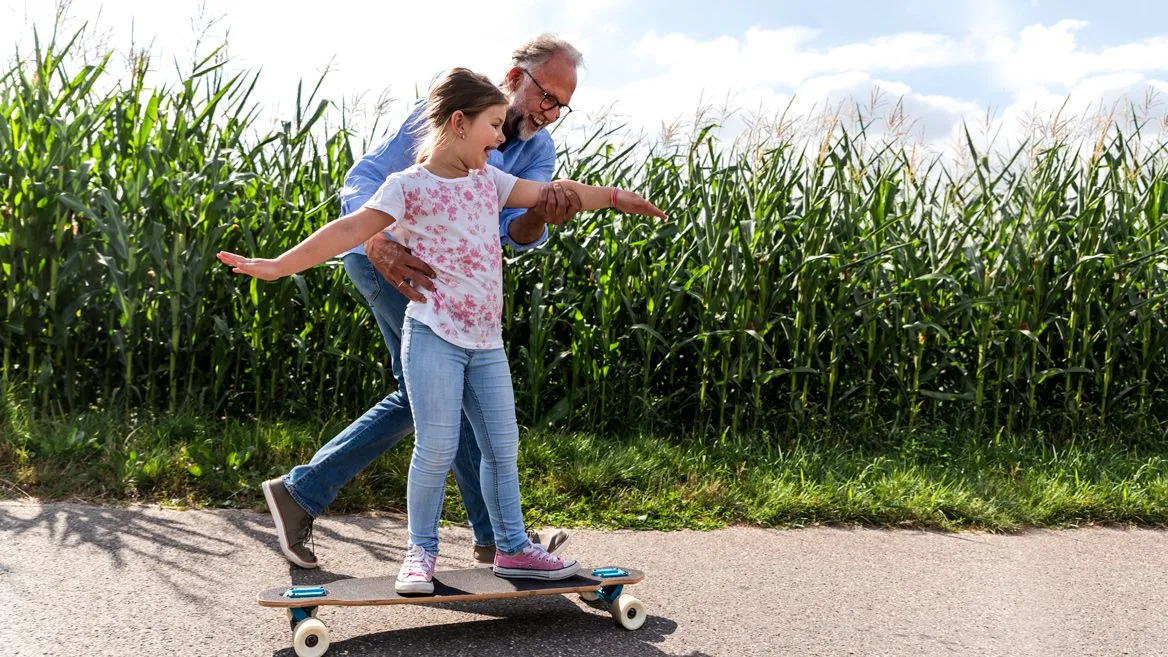 A dad guiding his daughter on a skateboard