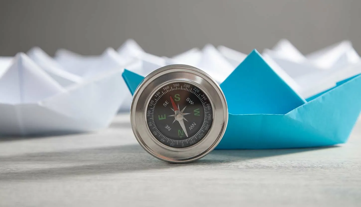 Compass in front of blue and white paper ships
