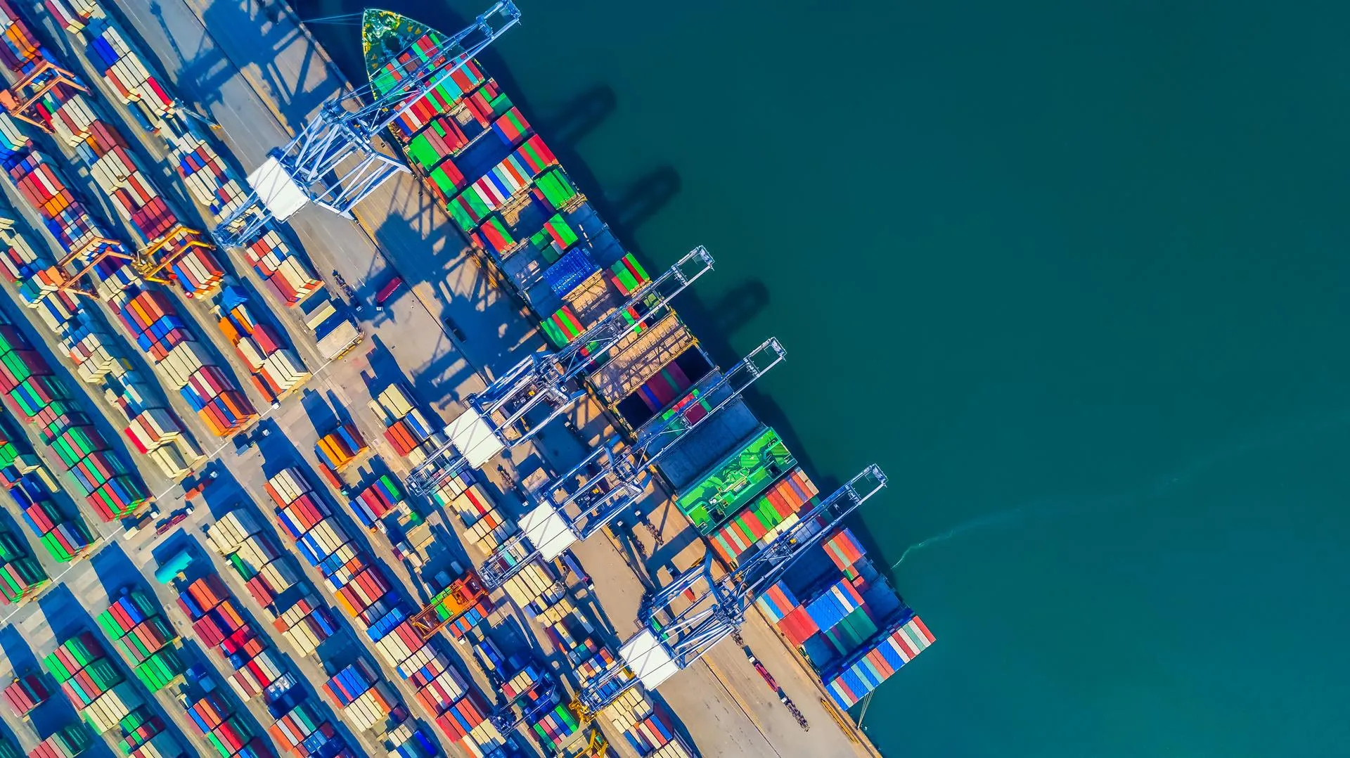 An aerial view of a containership docked in a container yard.