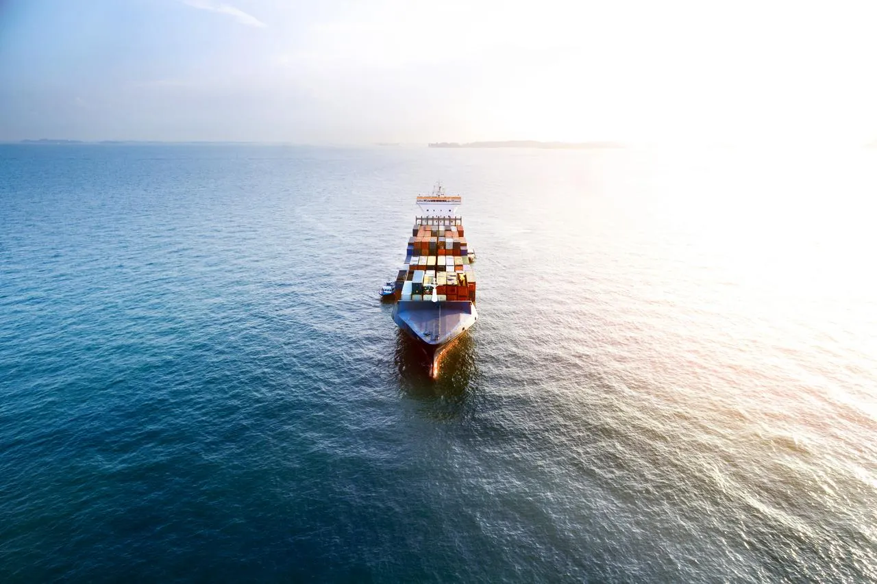 Aerial view of a container vessel front with sun and harbour in the back