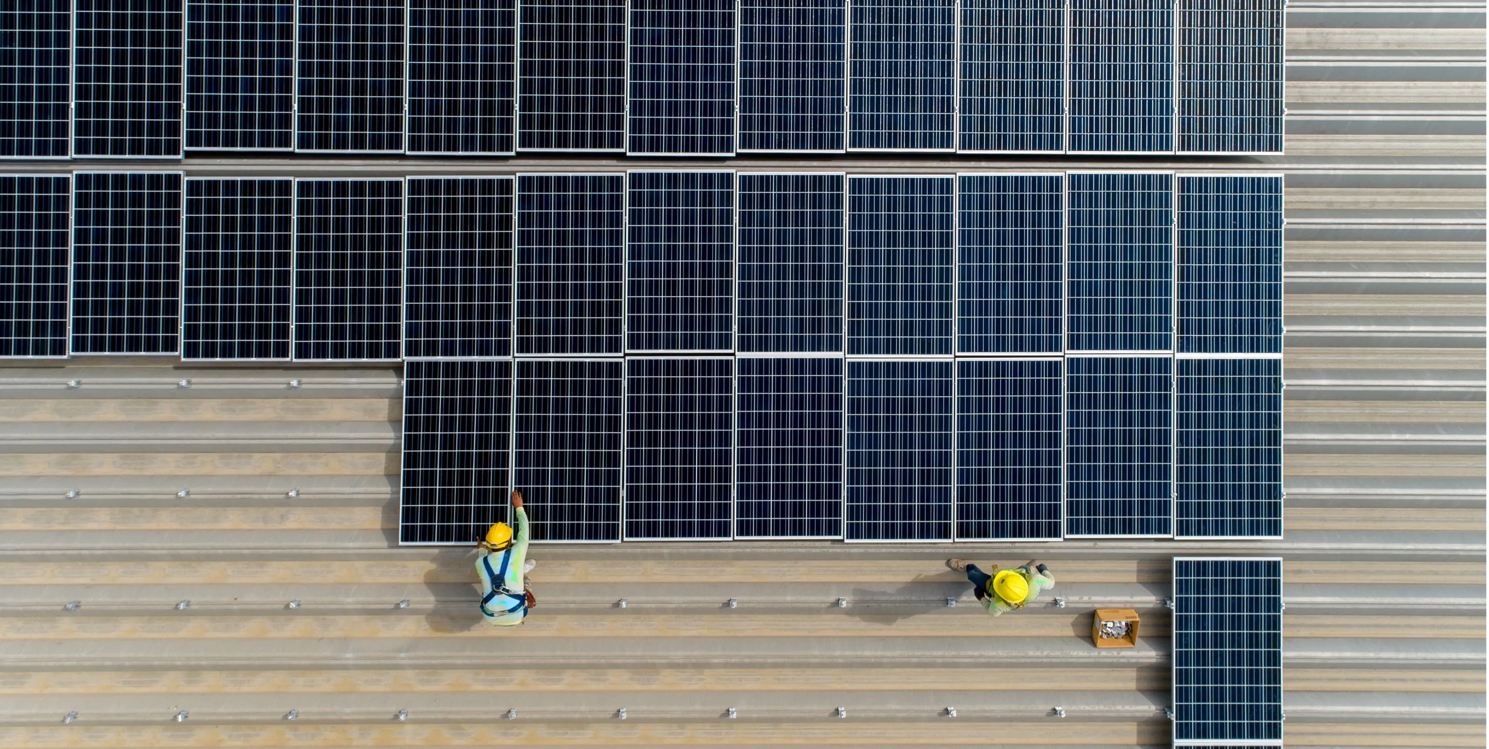 Two workers installing solar panels on a large rooftop