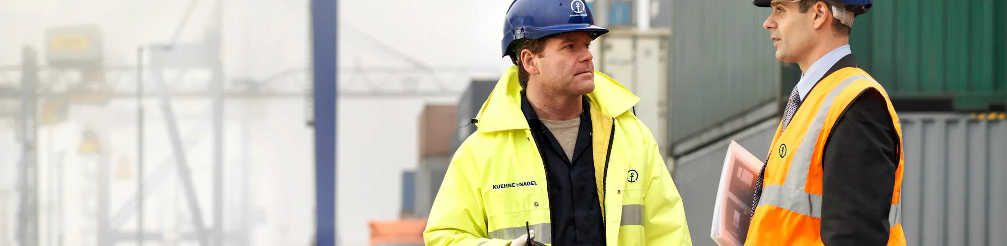 Two Kuehne+Nagel workers are talking next to some containers.